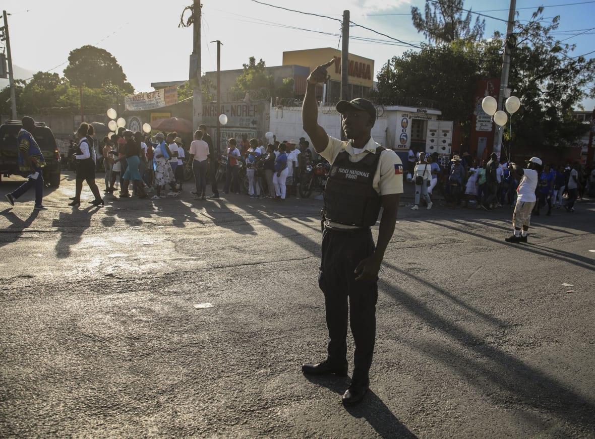 A national police officer raises his hand on a street in Haiti