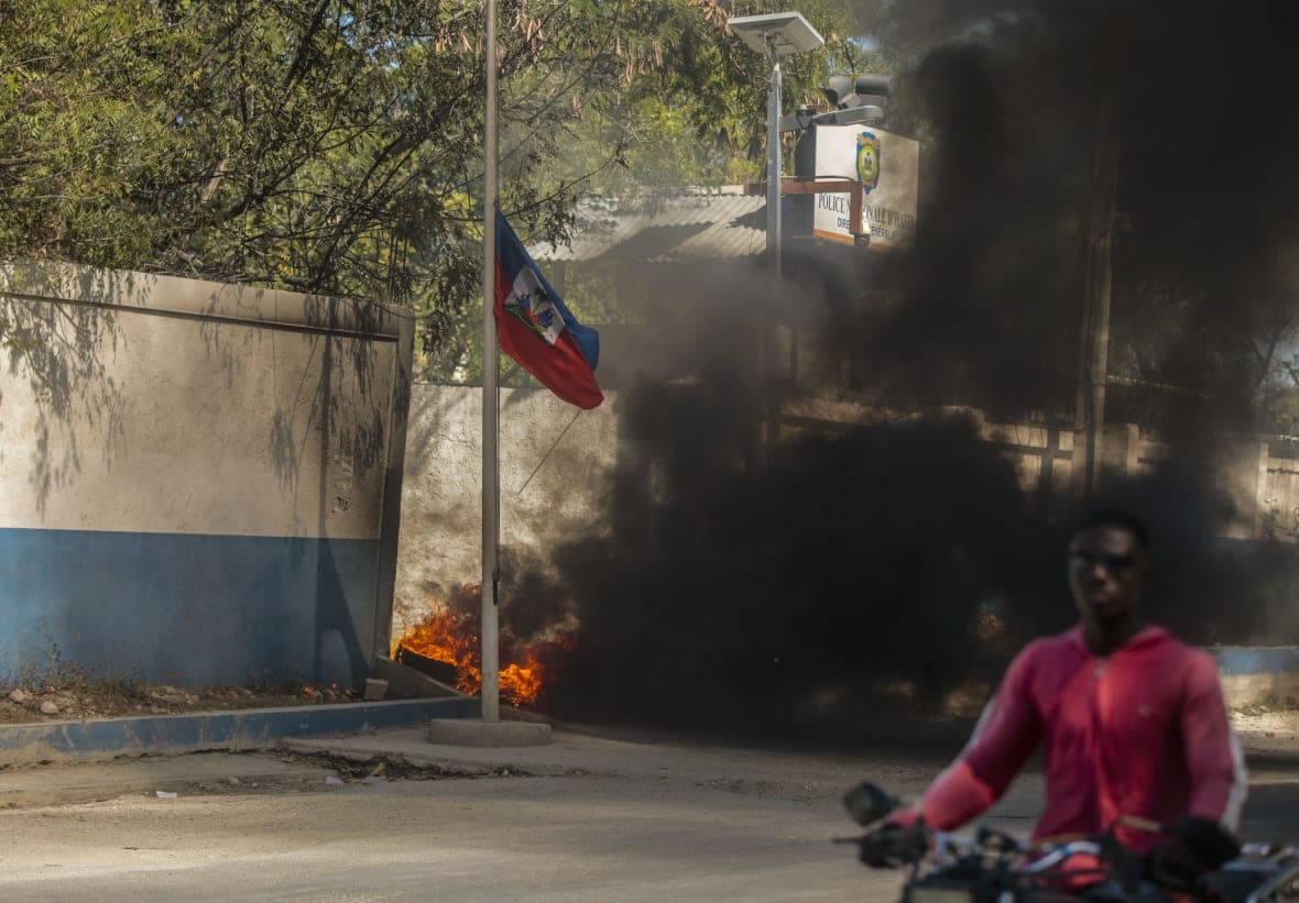 A Haitian flag at half-staff with a cloud of black smoke from a burning tire behind it