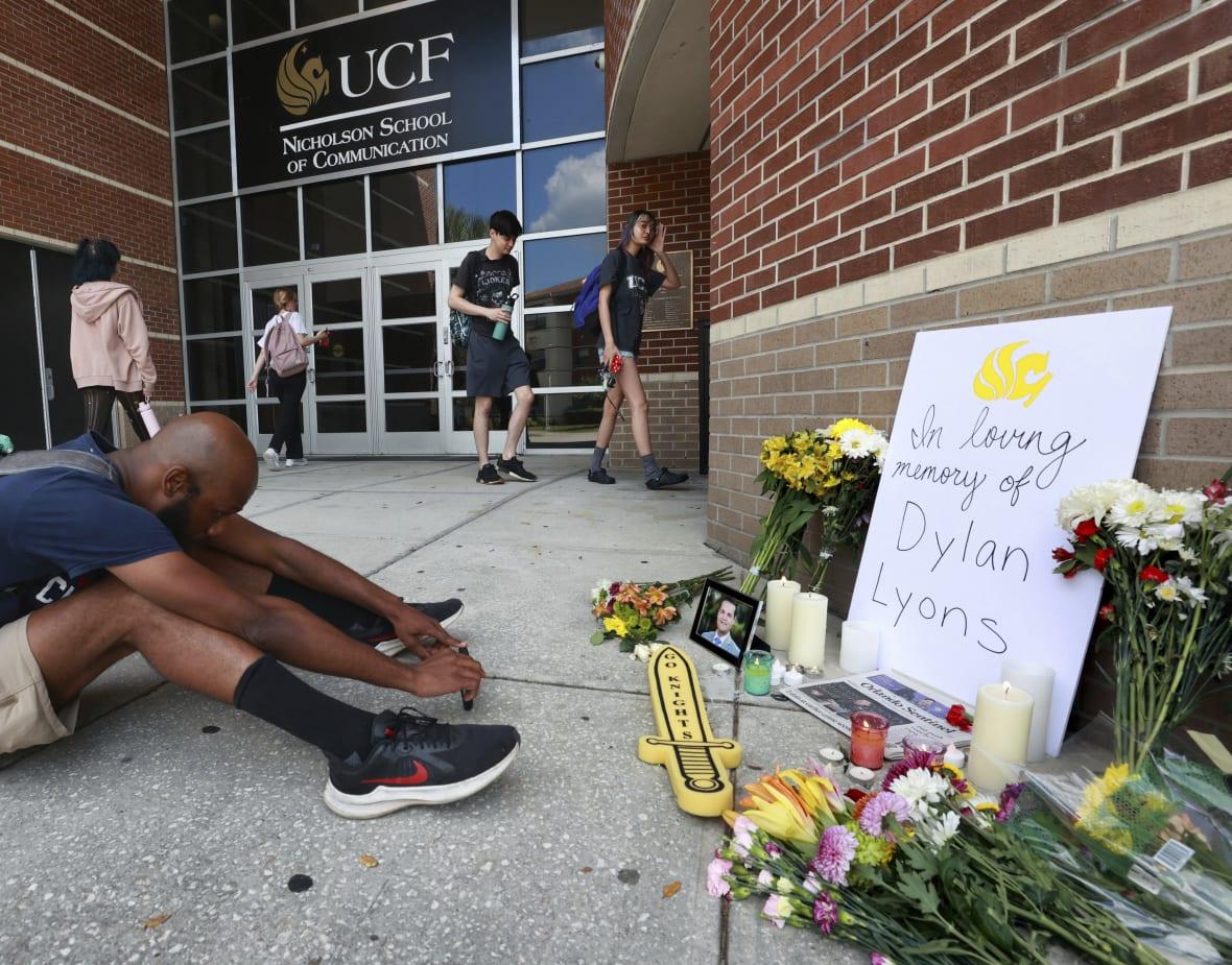 A person sits in front of the pop-up memorial for slain Spectrum News 13 journalist Dylan Lyons