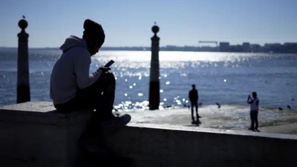 A young man checks his phone by a river