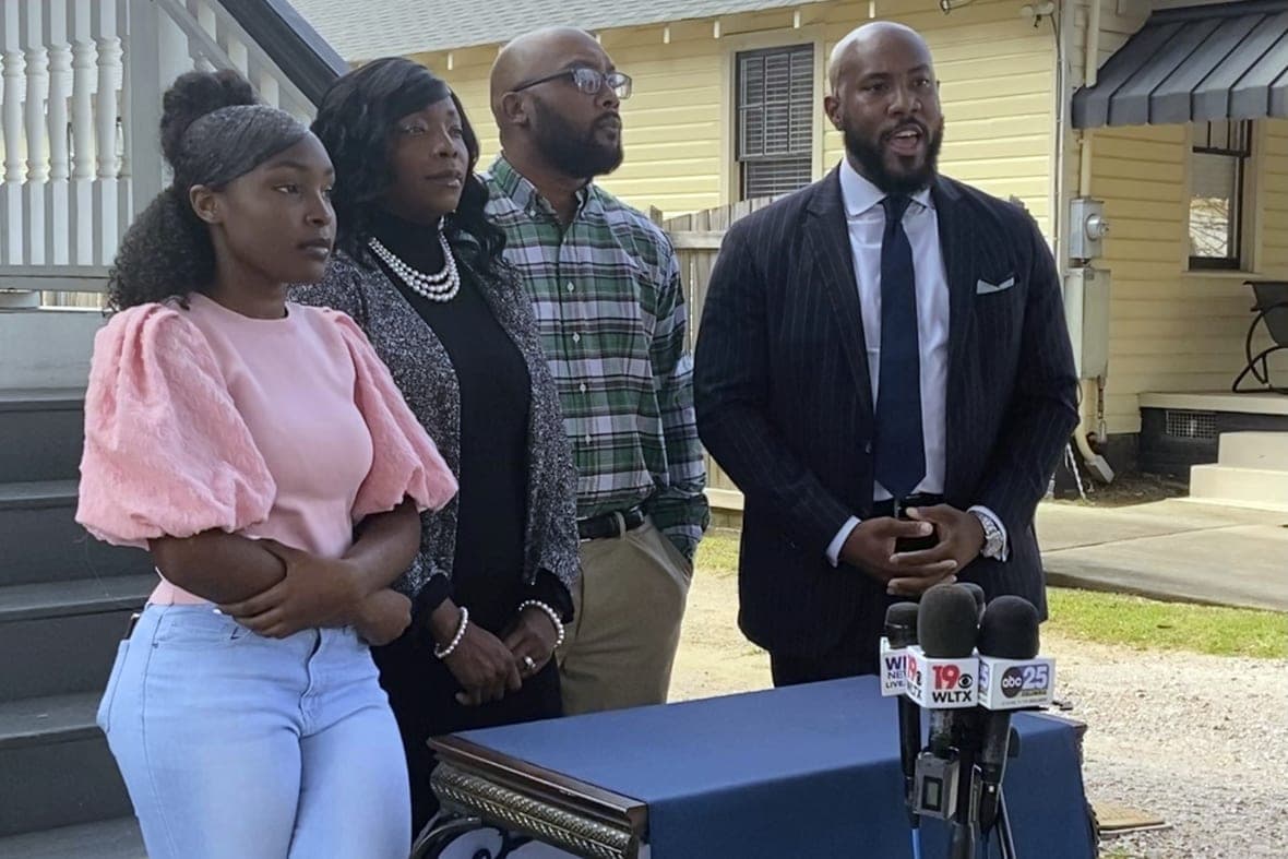 Marissa Barnwell with her parents and lawyer Tyler Bailey standing before a table with microphones