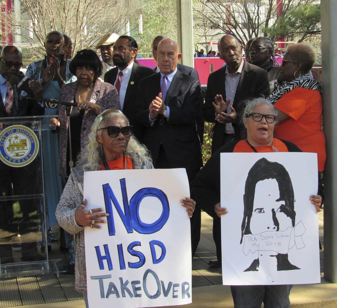 Protesters hold up signs at a news conference