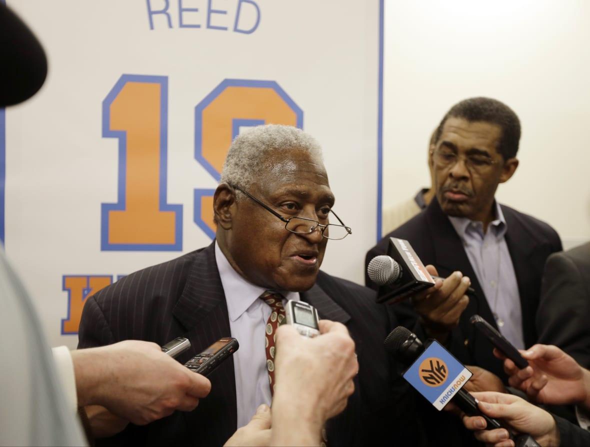 New York Knicks Hall-of-Famer Willis Reed, wearing a brown suit and brown patterned tie, takes questions from reporters