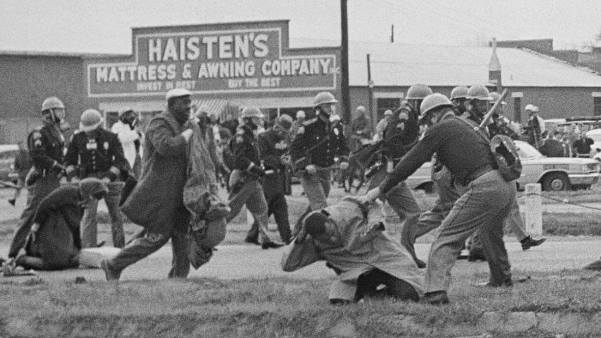 An Alabama state trooper swings a billy club at John Lewis in 1965