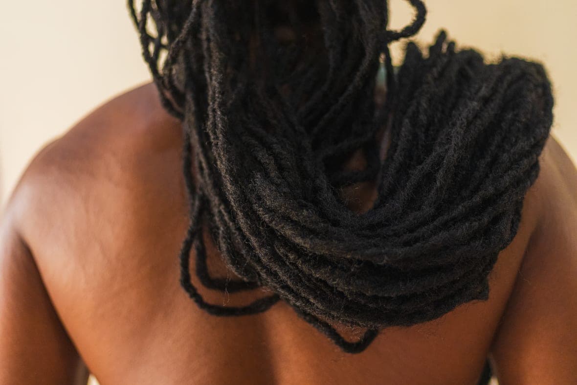 The back of a person with long dreadlocks pulled over their shoulder