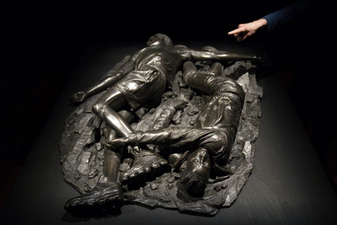 A woman points at a bronze sculpture by Kehinde Wiley titled “Death of Two Soldiers”