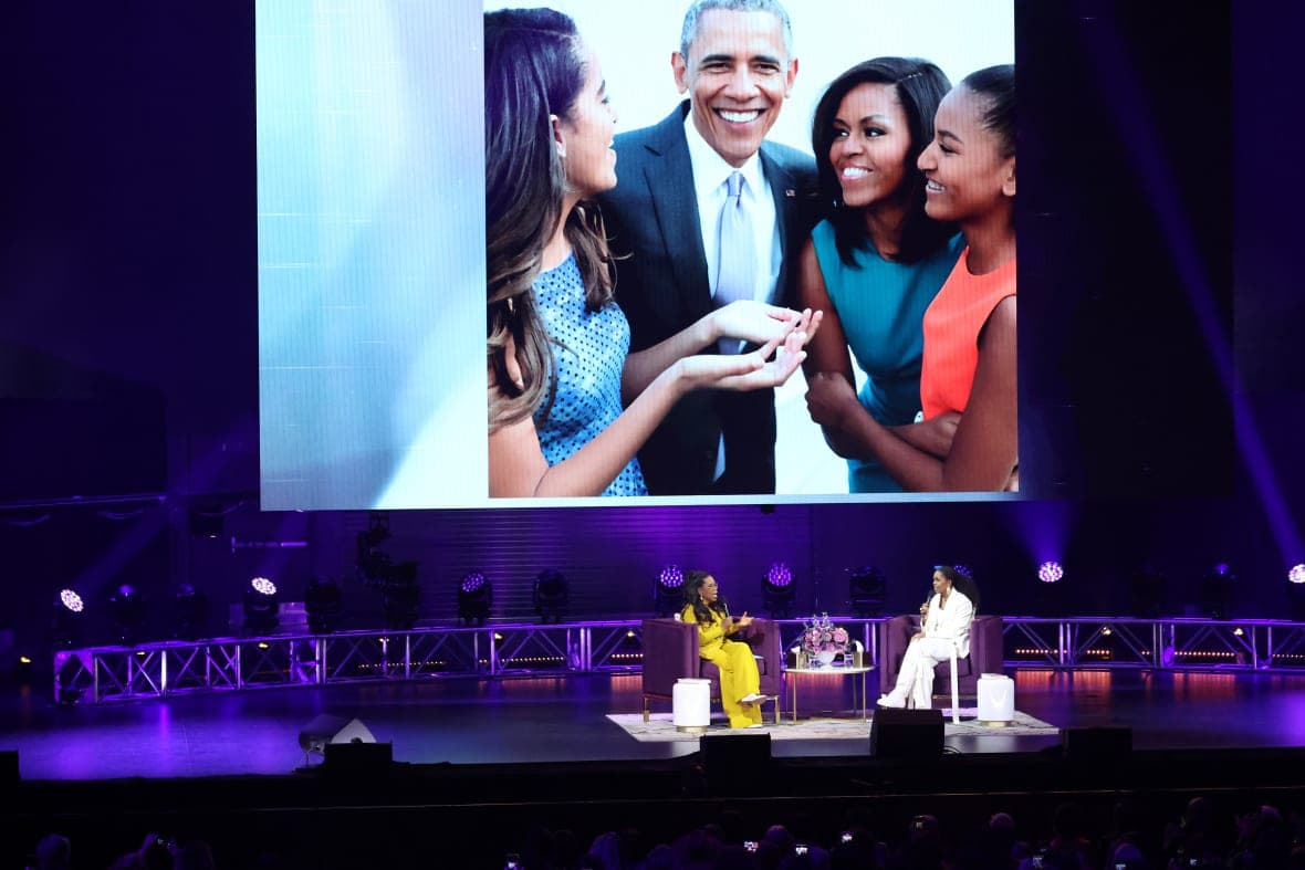 TV personality Oprah Winfrey and former First Lady Michelle Obama on stage before a screen showing the Obama family