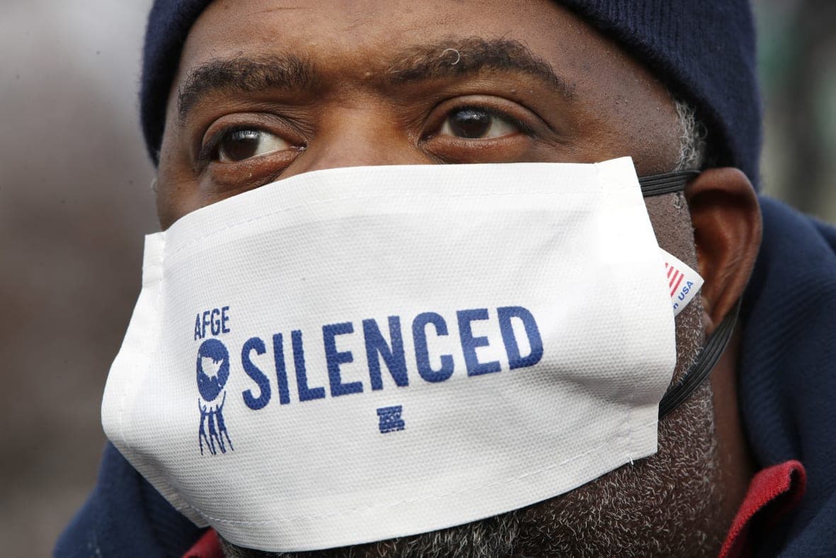 In a mask that says “silenced,” Appollos Baker, with the American Federation of Government Employees, protests