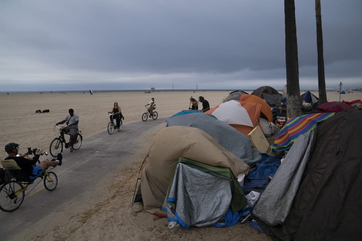 People ride their bikes past a homeless encampment set up along the boardwalk