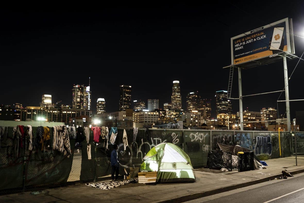 A homeless person’s tent is backdropped by the skyline of Los Angeles