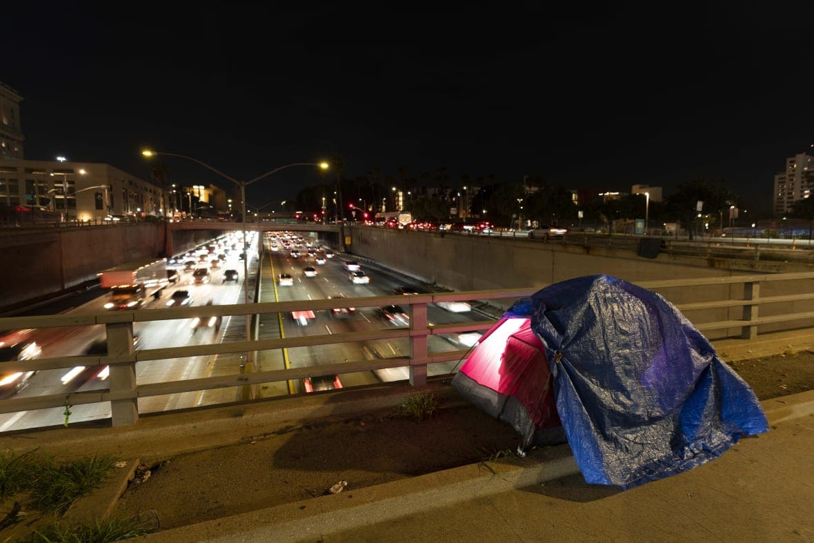A tarp covers a portion of a homeless person’s tent on a bridge