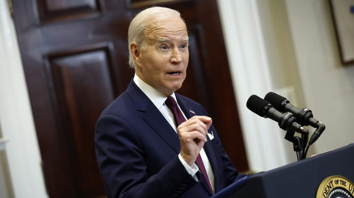 President Joe Biden gestures while standing at a podium wearing a navy jacket and maroon tie