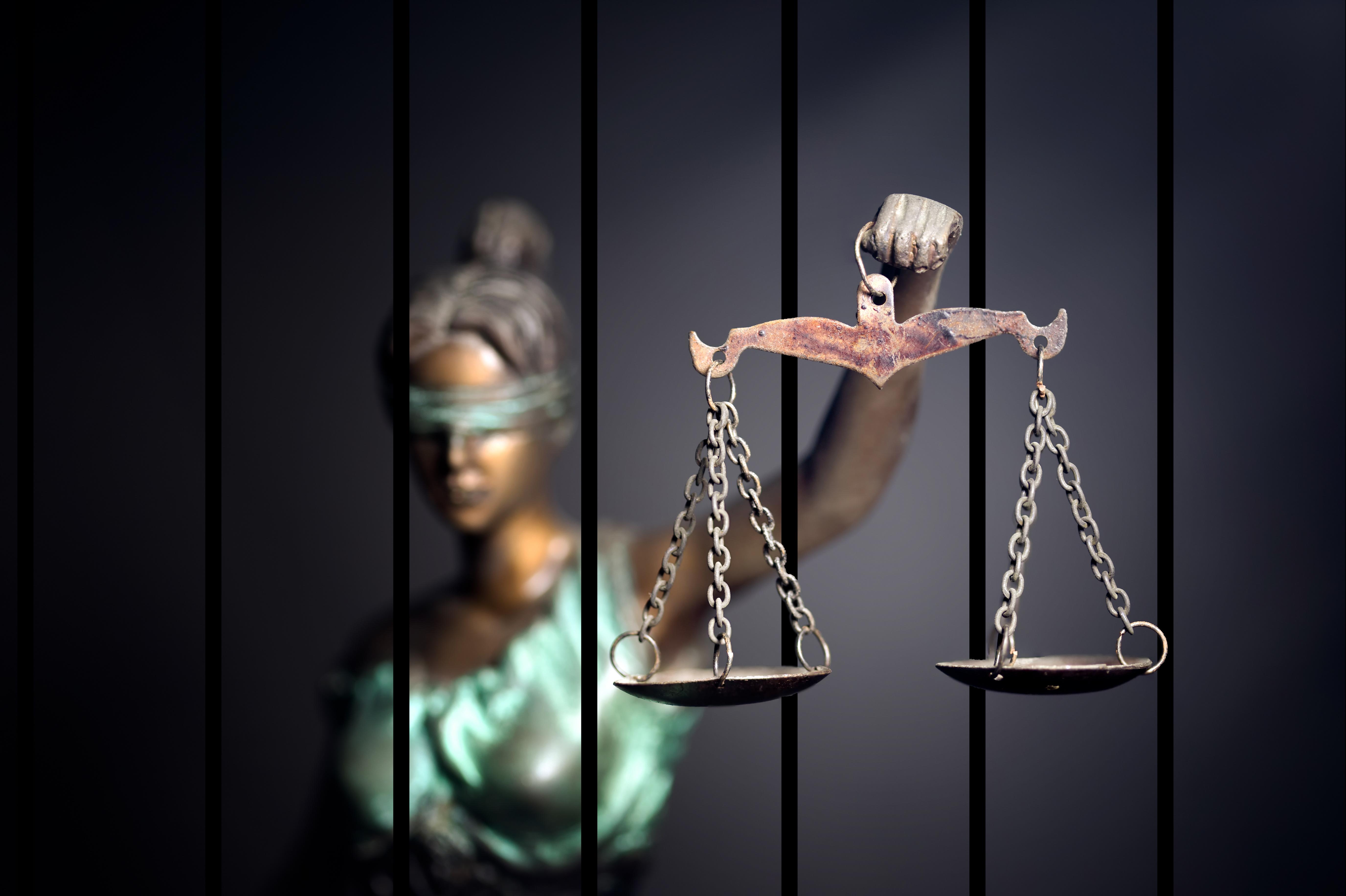 A statue of blindfolded Justice holding her scales from behind bars