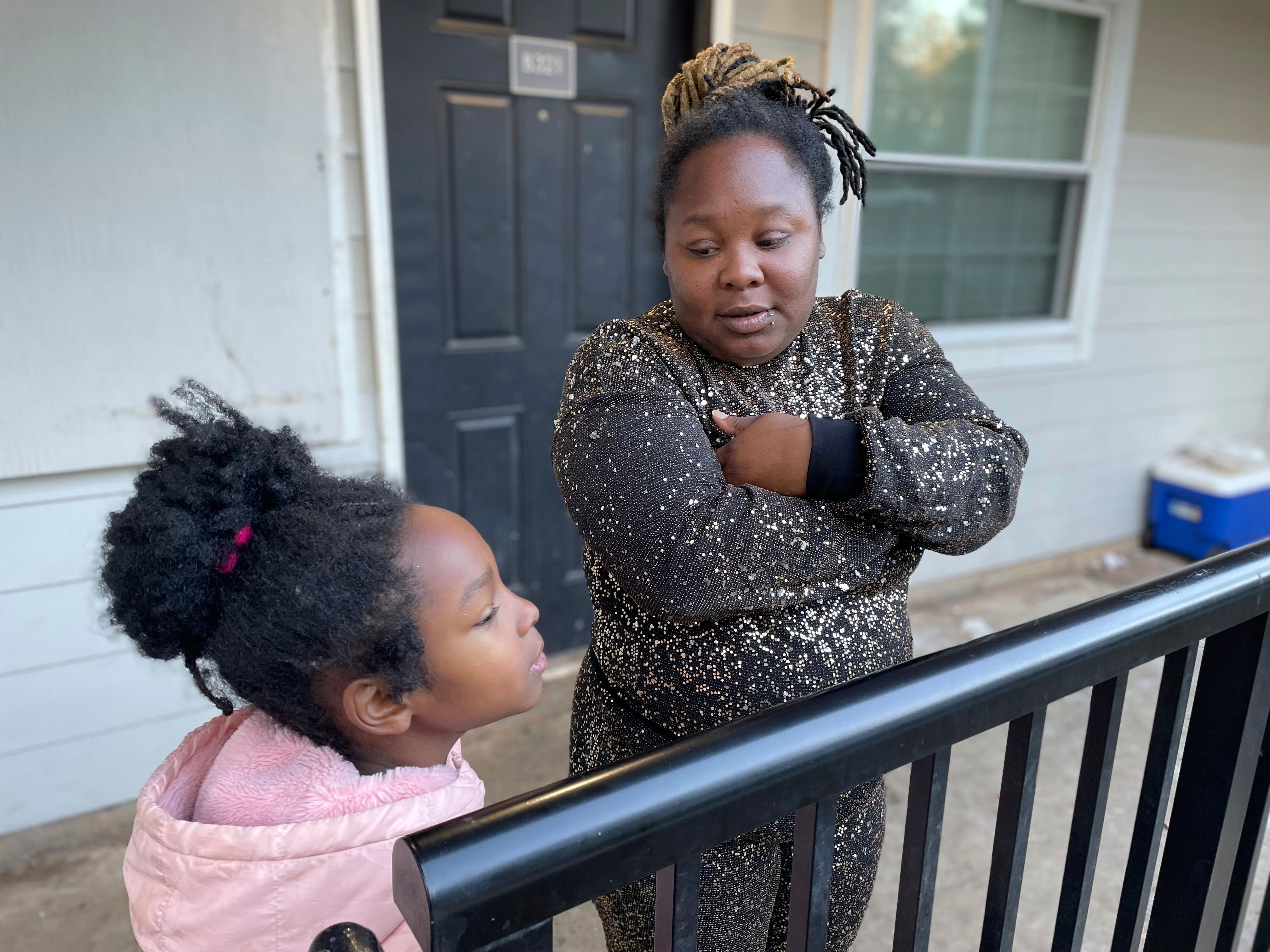 A young girl and her mother Tameka stand on a porch by a black railing