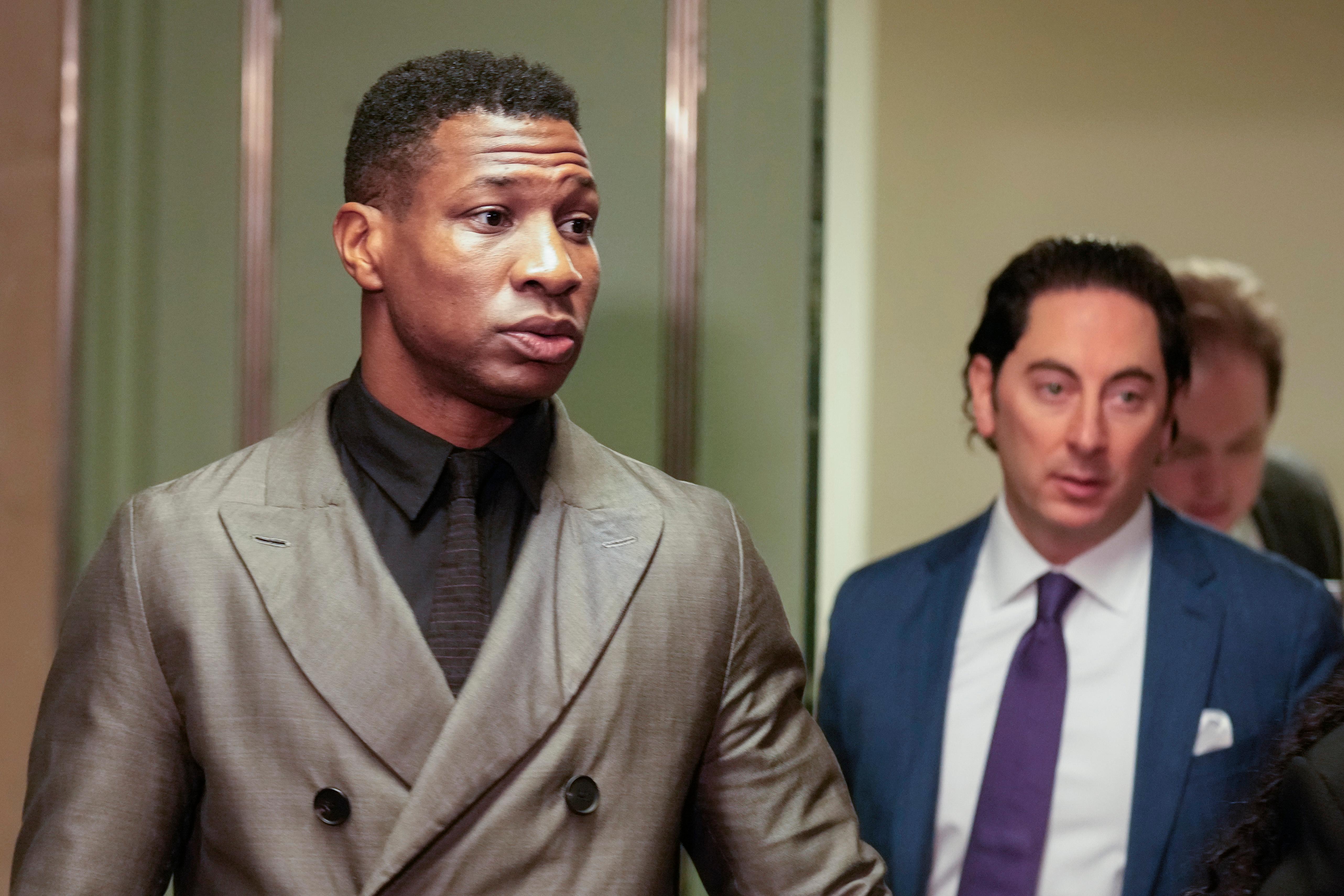 Actor Jonathan Majors wearing a gray coat and black shirt in a courtroom