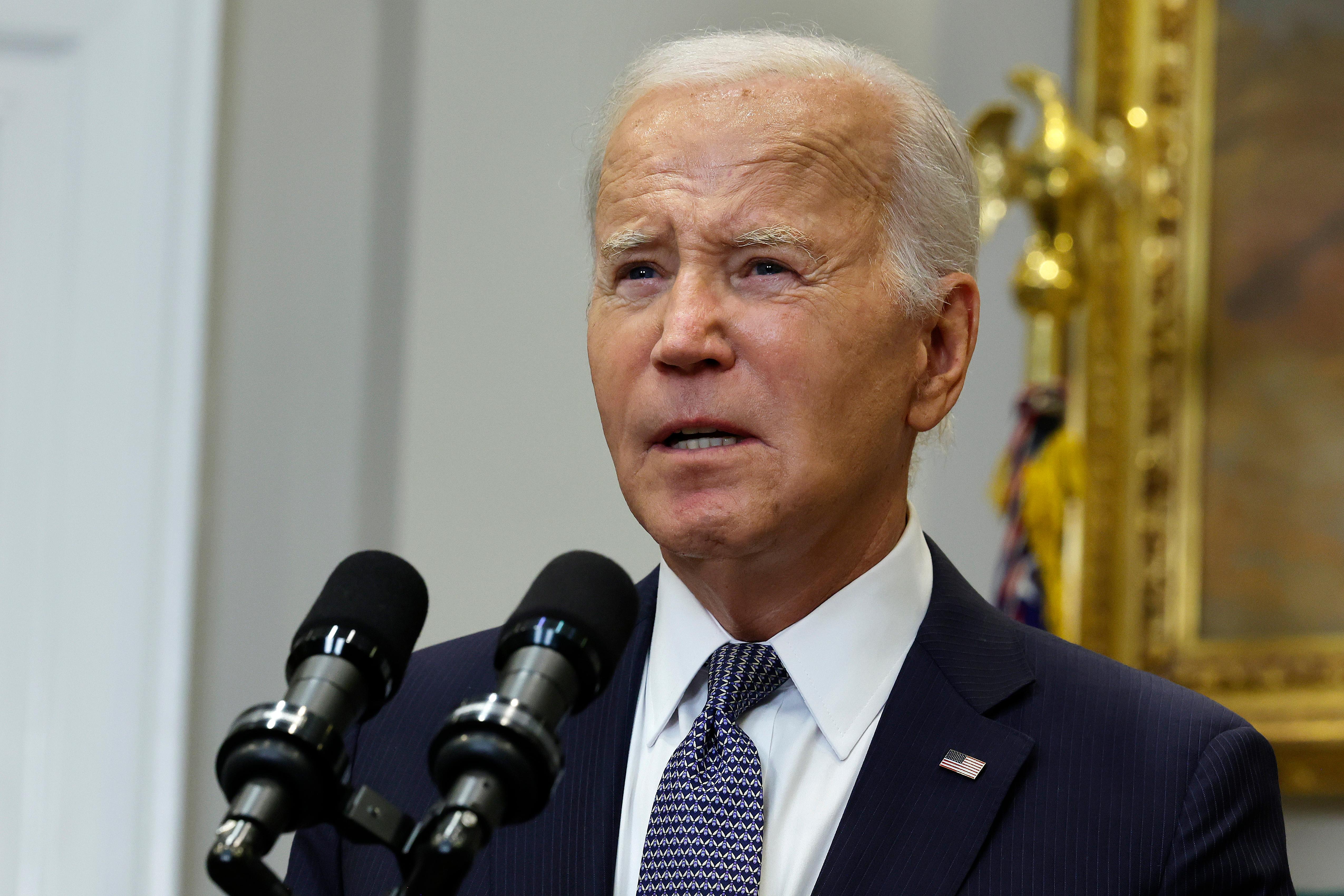 President Joe Biden stands behind a microphone wearing a dark blue jacket and blue patterned tie