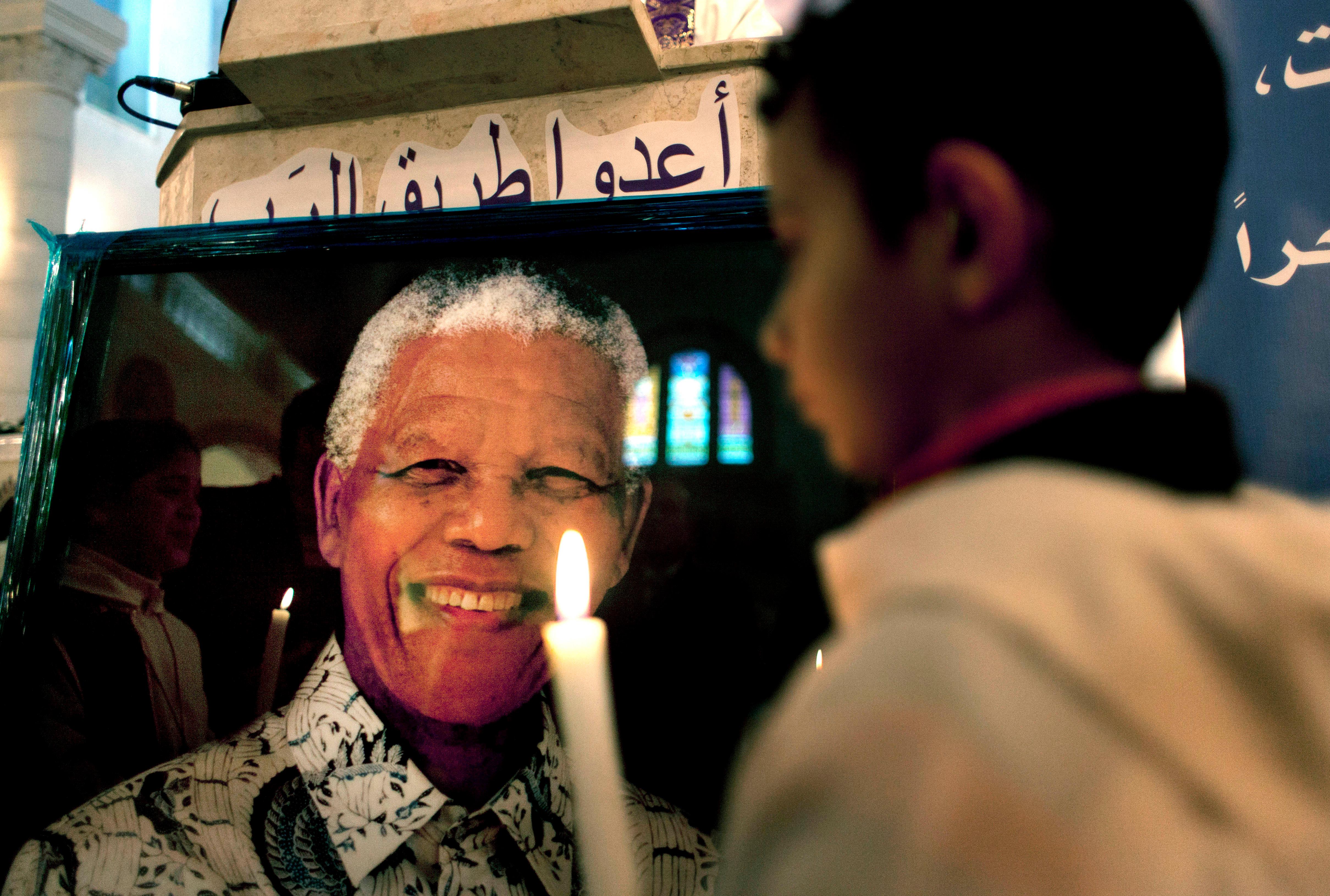 A Palestinian child holds a lit candle as he prays in front of a poster of late South African leader Nelson Mandela