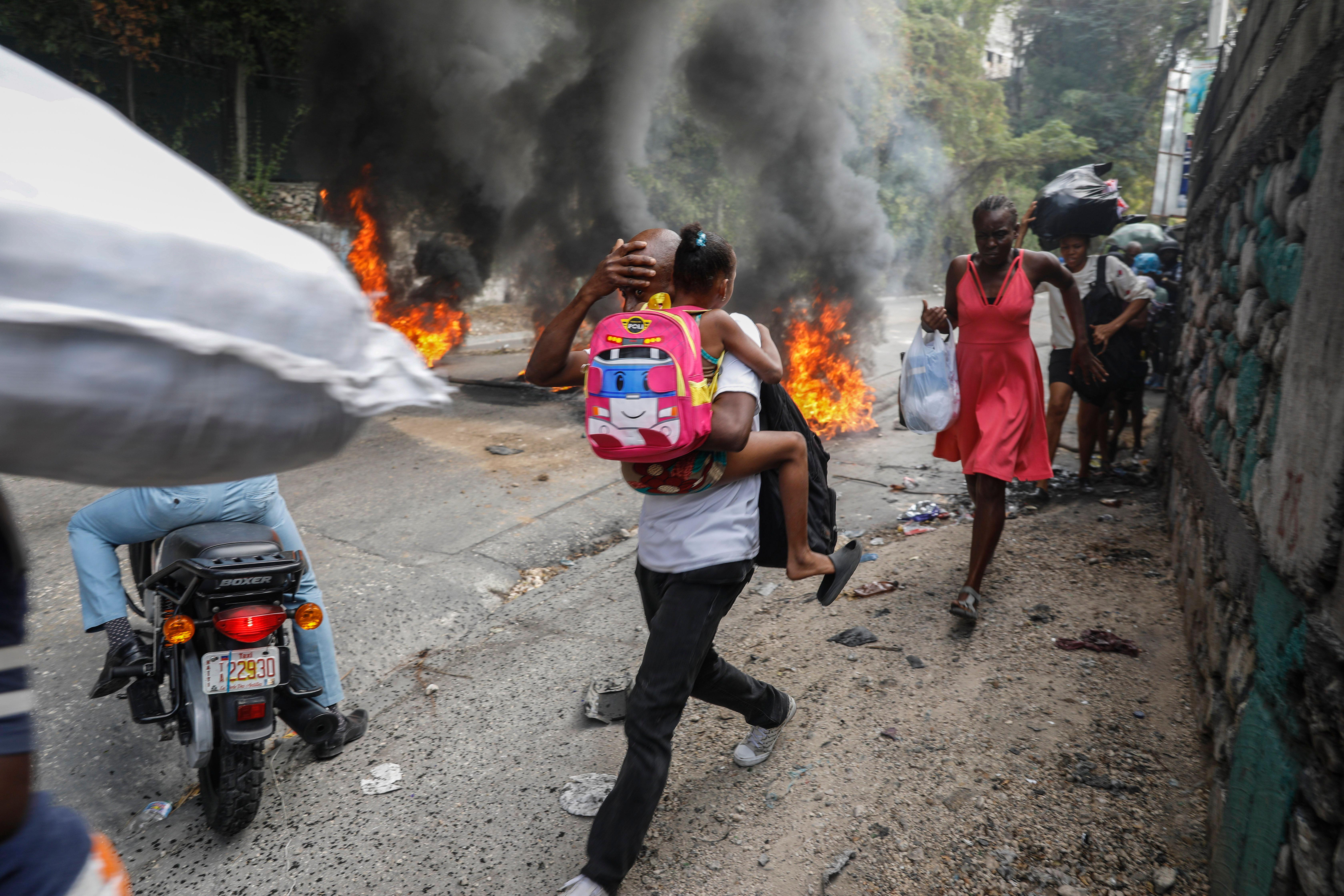 People walk past burning tires during a protest against Haitian Prime Minister Ariel Henry