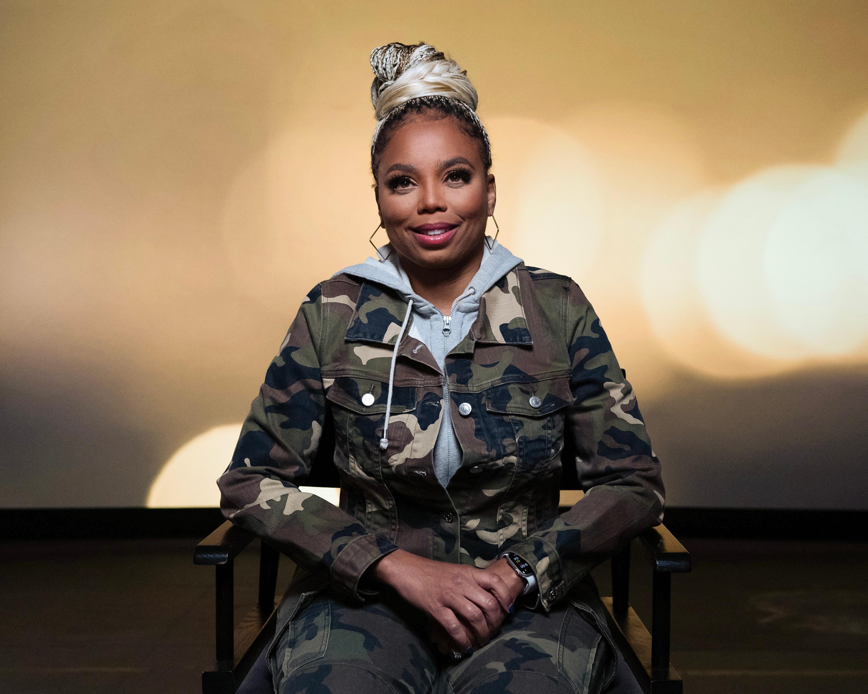 Sports journalist Jemele Hill sits in a chair wearing a camouflage jacket and pants