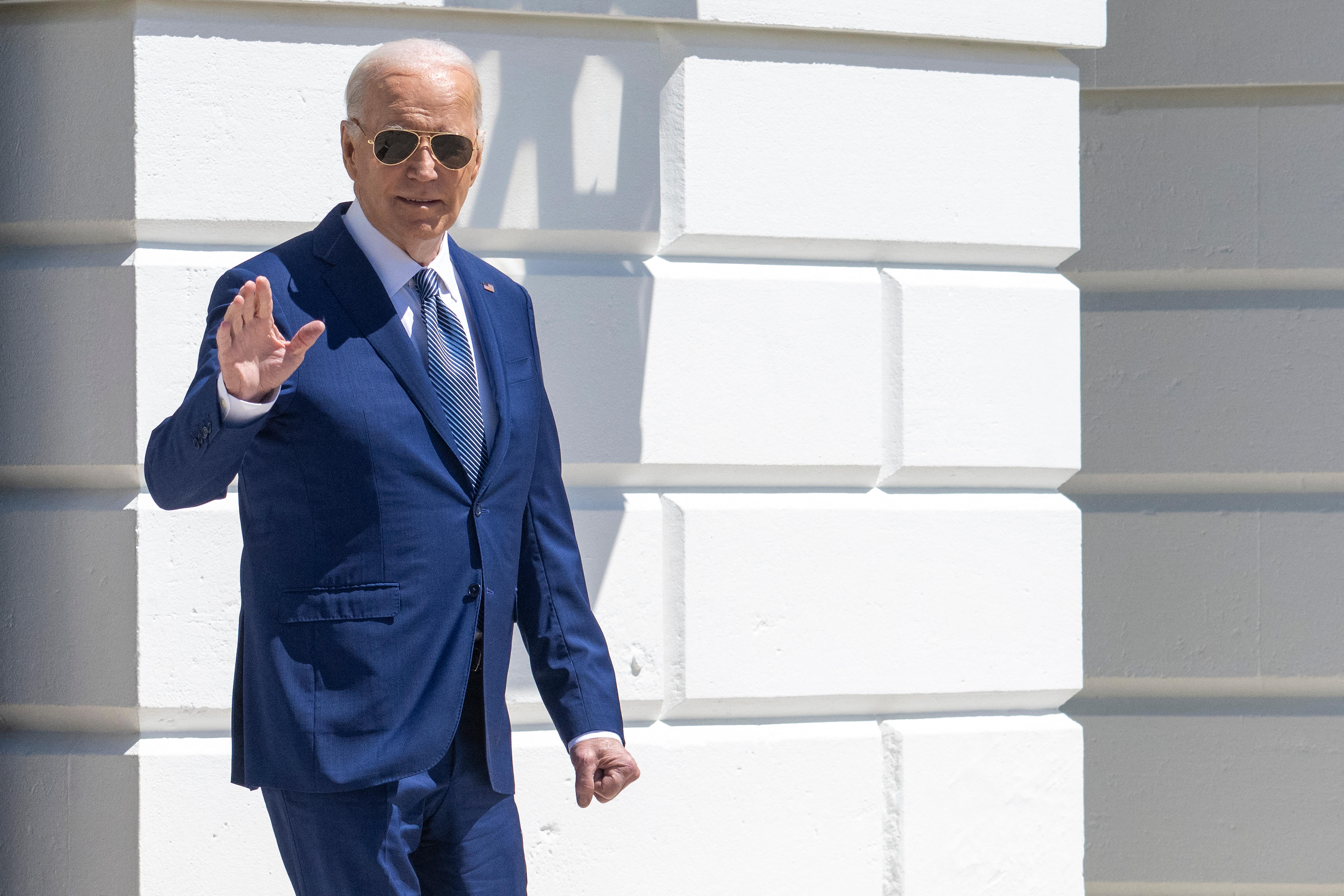 President Joe Biden waves, wearing a blue suit and blue-striped tie