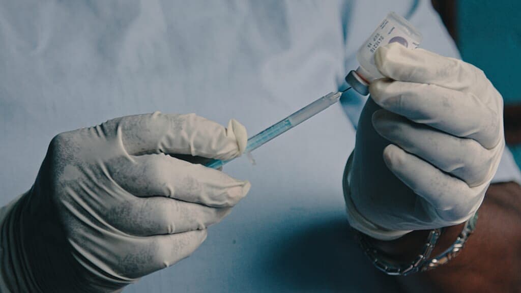 Hands in medical gloves put vaccine into a syringe