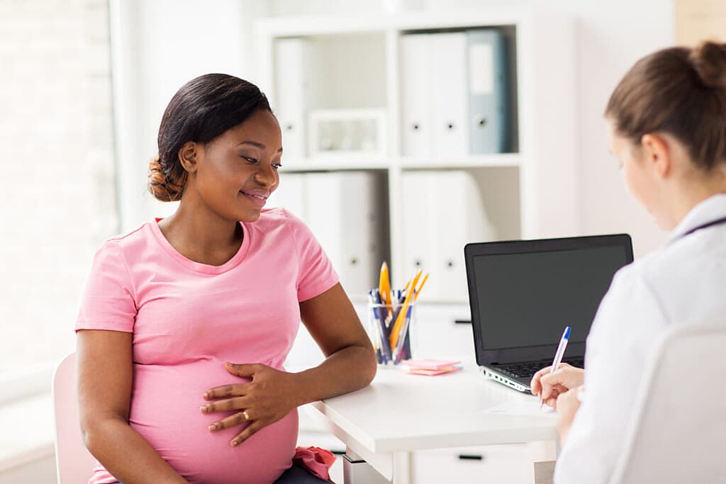 A pregnant woman holds her belly as a medical worker holds a pen by a laptop