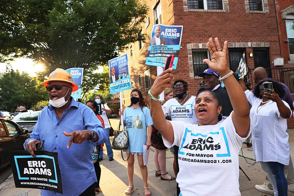 A group of people wear T-shirts and hold signs supporting New York City mayoral candidate Eric Adams