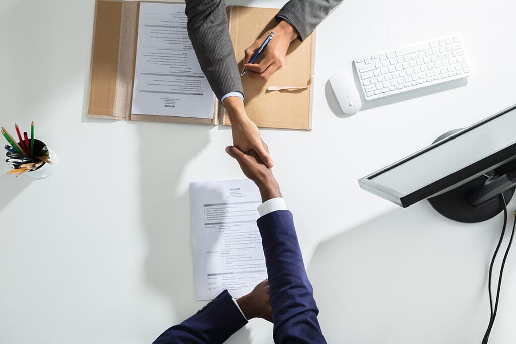 Two people shake hands across a desk