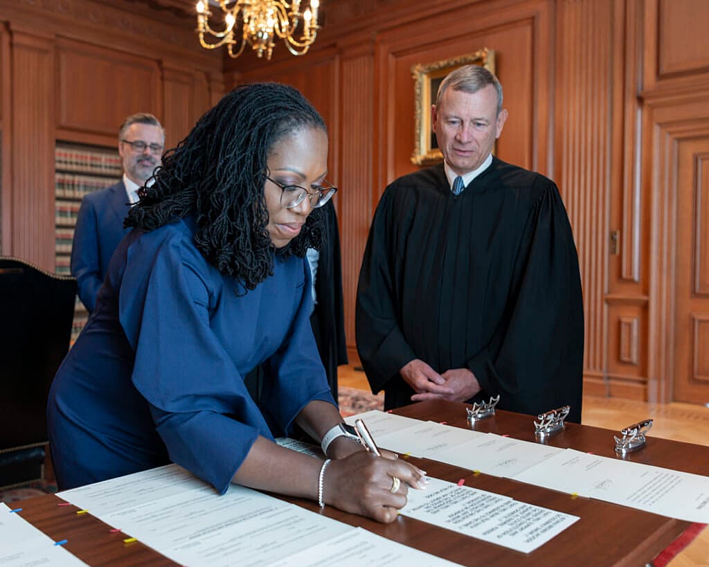Chief Justice John G. Roberts, Jr. (right) looks on as Justice Ketanji Brown Jackson signs the Oaths of Office