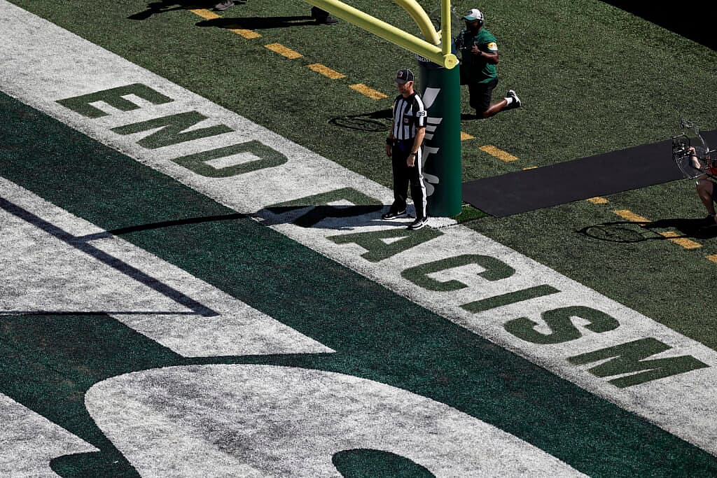 Back judge Rich Martinez stands in the end zone next to the social justice message “End Racism”