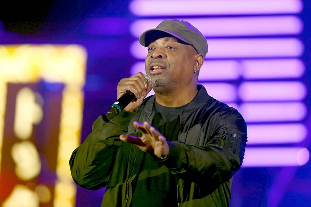 Rapper Chuck D of Public Enemy holding a microphone, wearing a gray baseball cap and black jacket