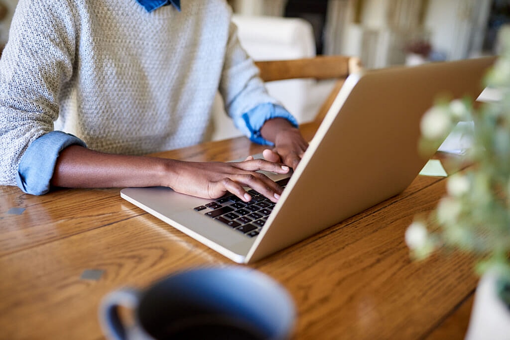 A person in a blue shirt and white sweater using a laptop on a wooden table