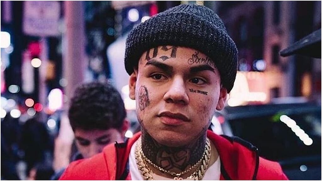 Rapper Tekashi 6ix9ine wearing a red jacket and black cap