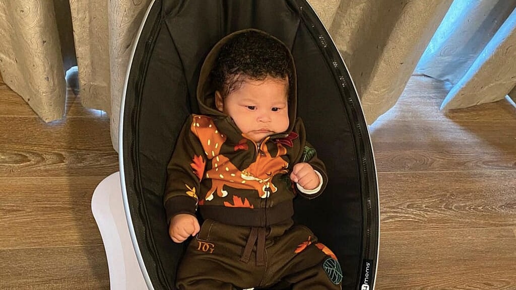 Rapper Nicki Minaj's infant son, dressed in a brown sweatsuit, is shown in a brown carseat