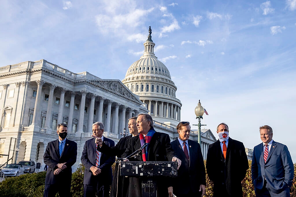 Republican Representative Andy Biggs of Arizona stands behind a podium wearing a black coat and colorful scarf