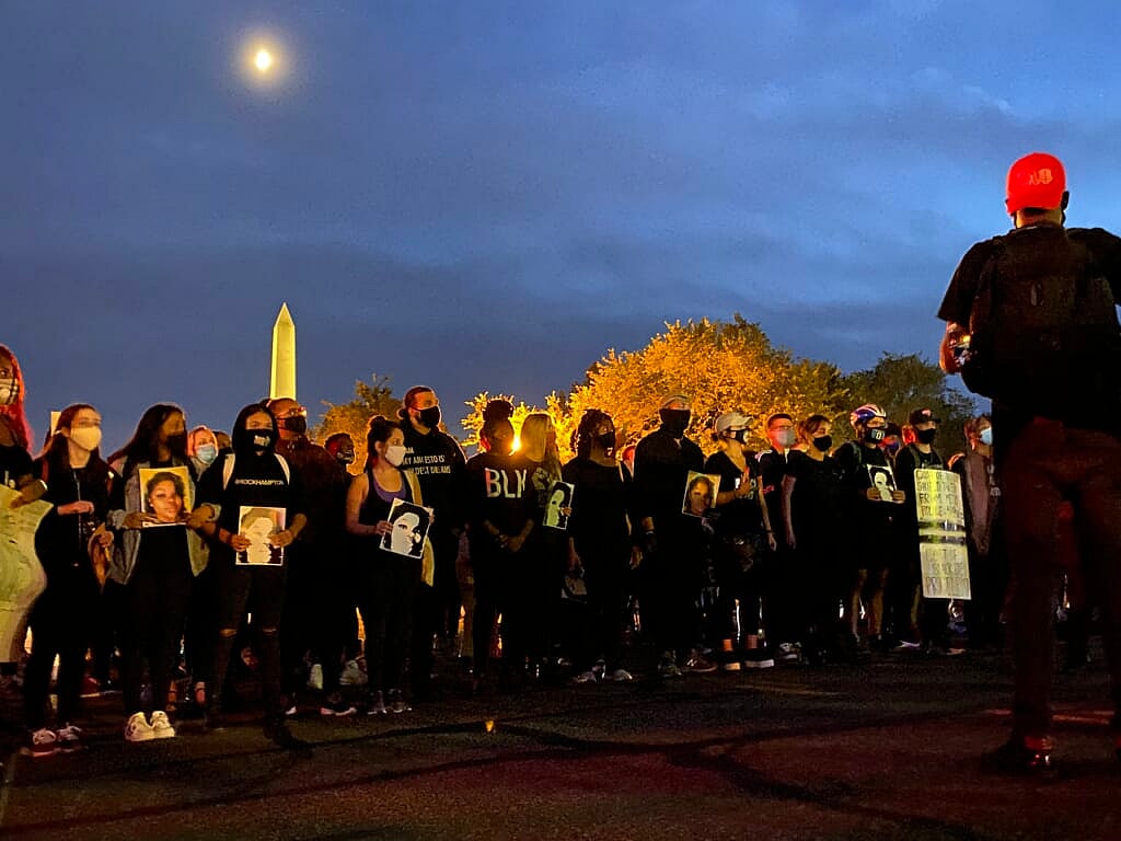 A group of demonstrators dressed in black stand before the Washington Memorial at night