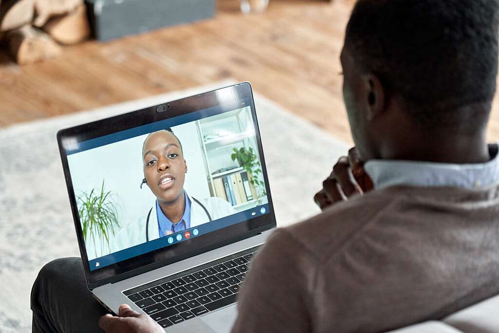 A man looks at a laptop screen showing a virtual therapist