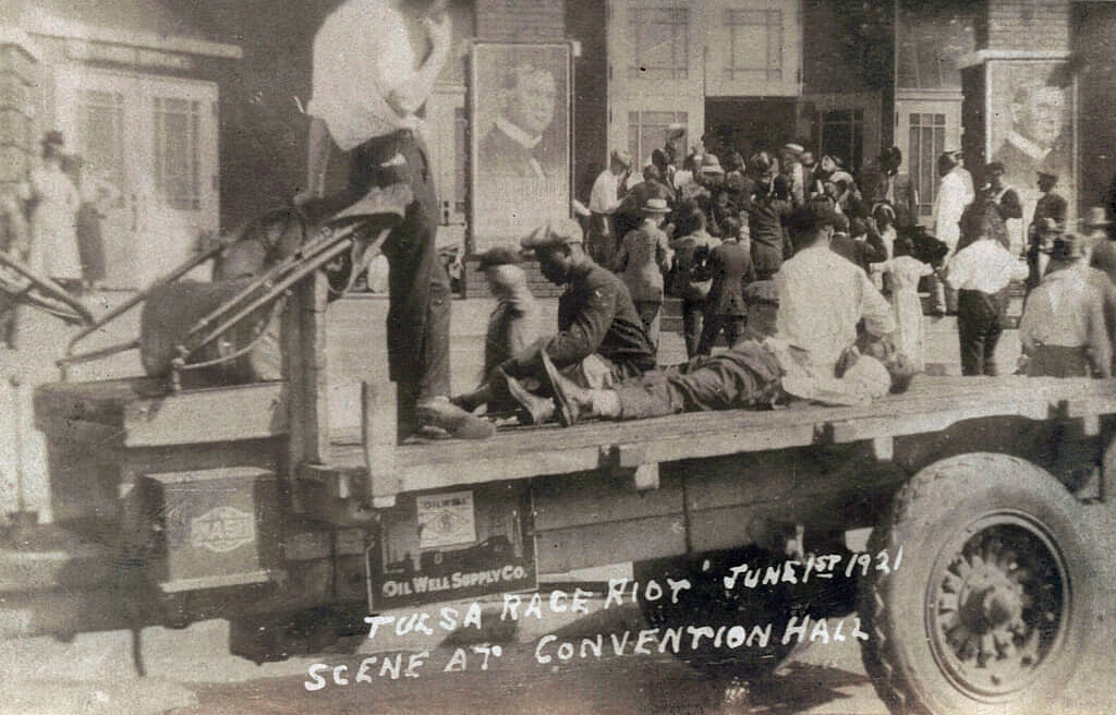 A truck parked in front of the Convention Hall with a man lying on the bed of a truck during the Tulsa Race Massacre