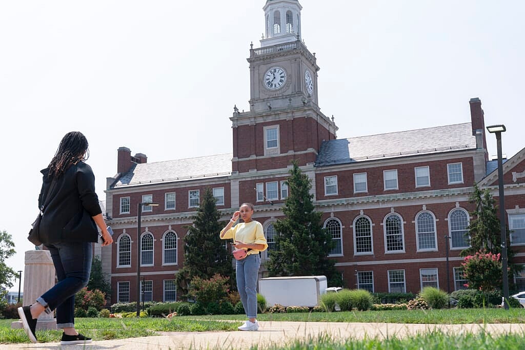 The Founders Library in the background, people walk along the Howard University campus 