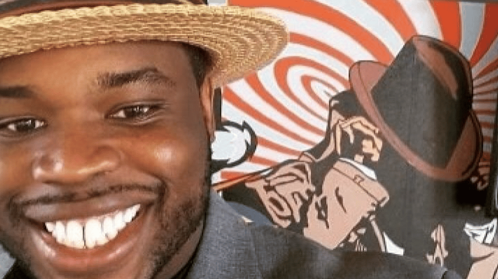 Vauhxx Booker, wearing a straw hat, stands in front of a background of a cartoon detective in a trenchcoat and hat