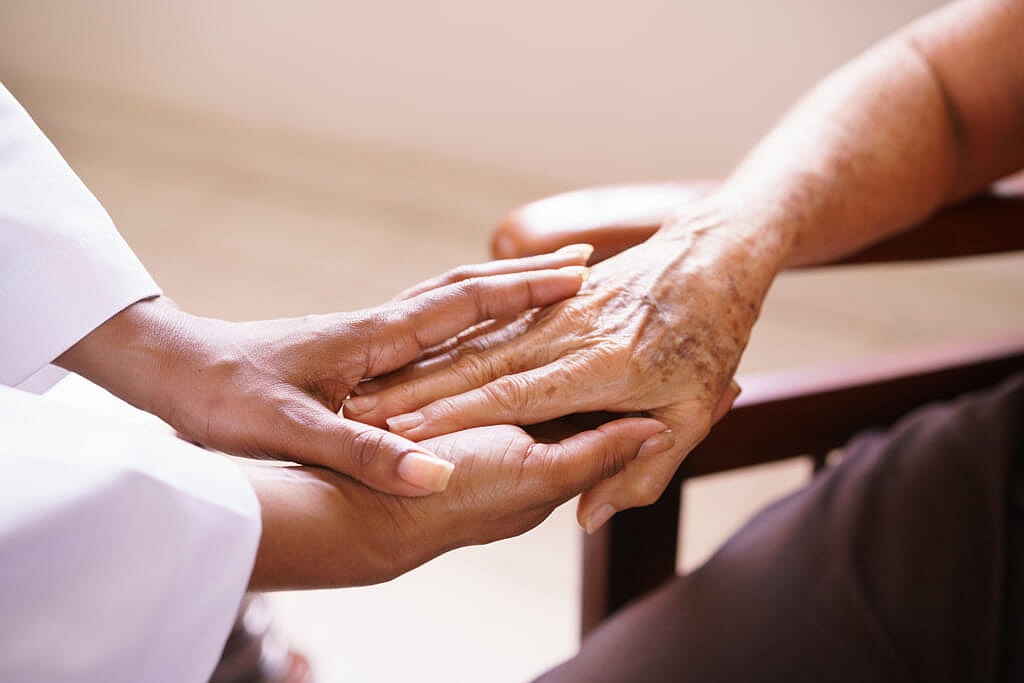 Home care attendant holds elderly person's hand