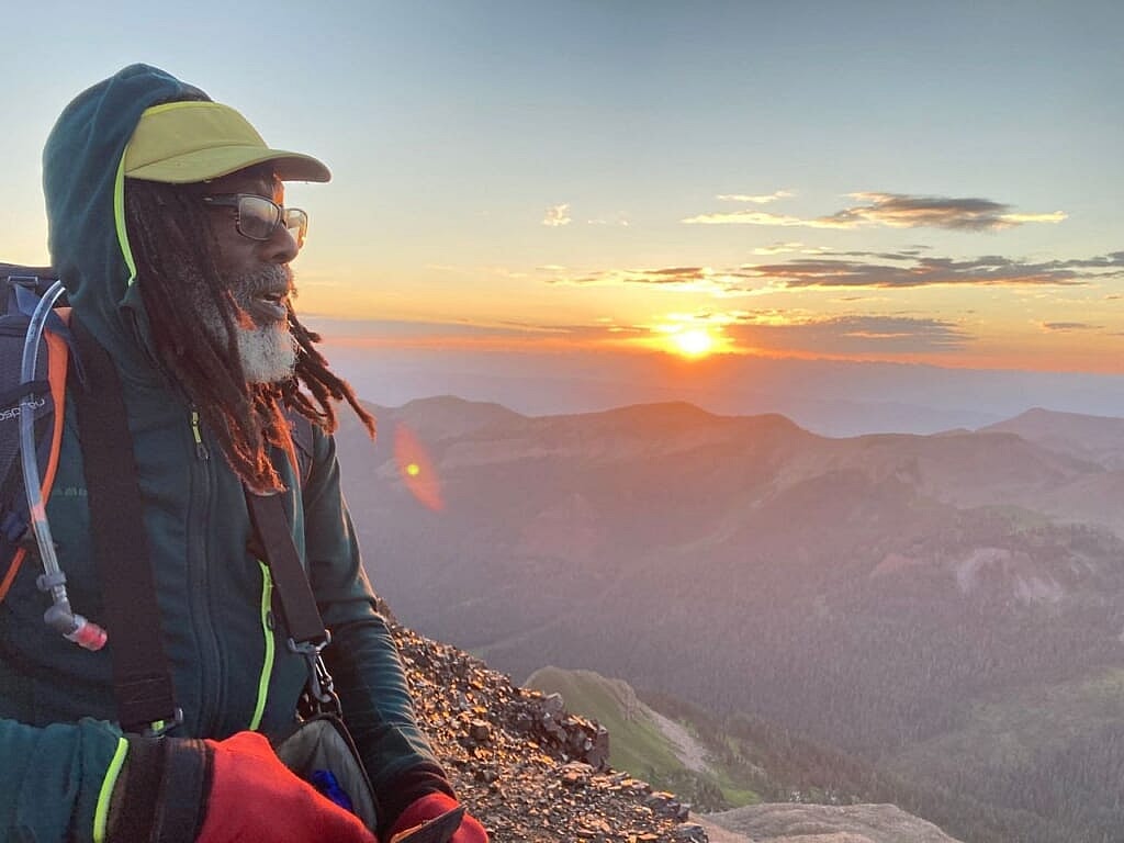 Mountain climber Phil Henderson watching a sunset atop a mountain