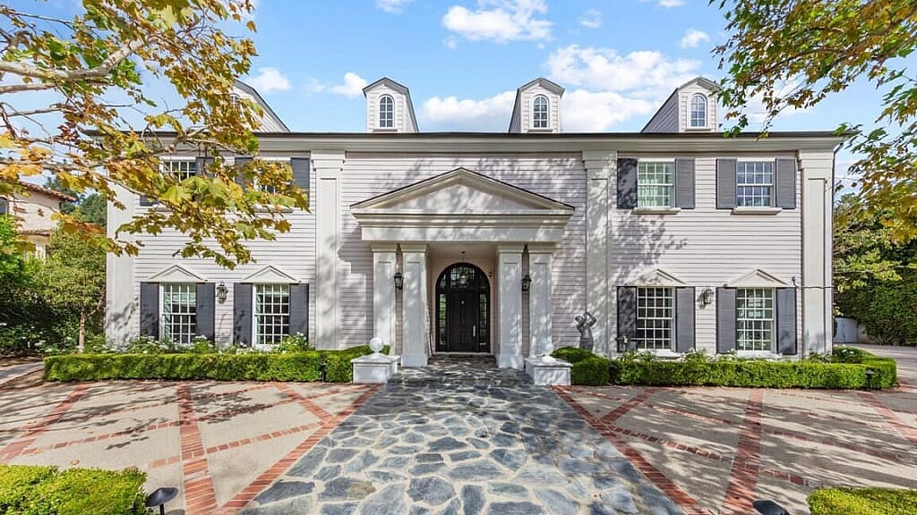 A mansion with white siding and gray shutters and a stone path leading up to the house