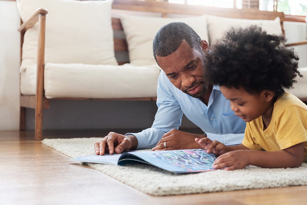 A father and child lie on the floor looking at a book