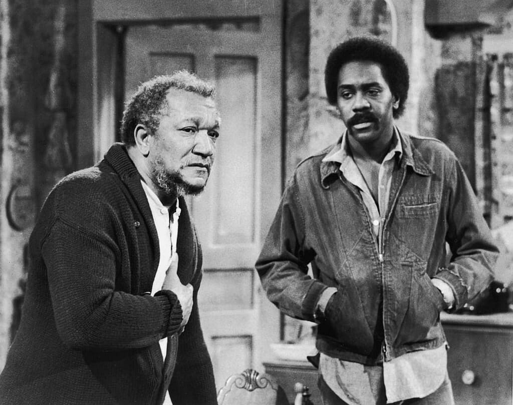 Actor Redd Foxx clutches his chest in "Sanford and Son" with Demond Wilson in this black-and-white photo.