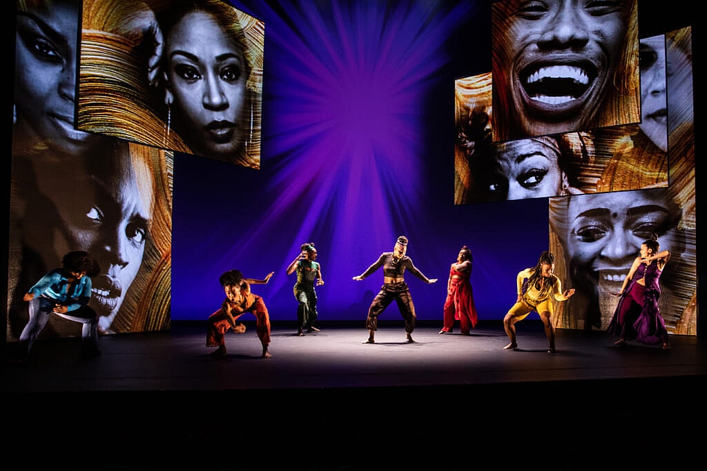 A stage with large photos of people's face and seven performers