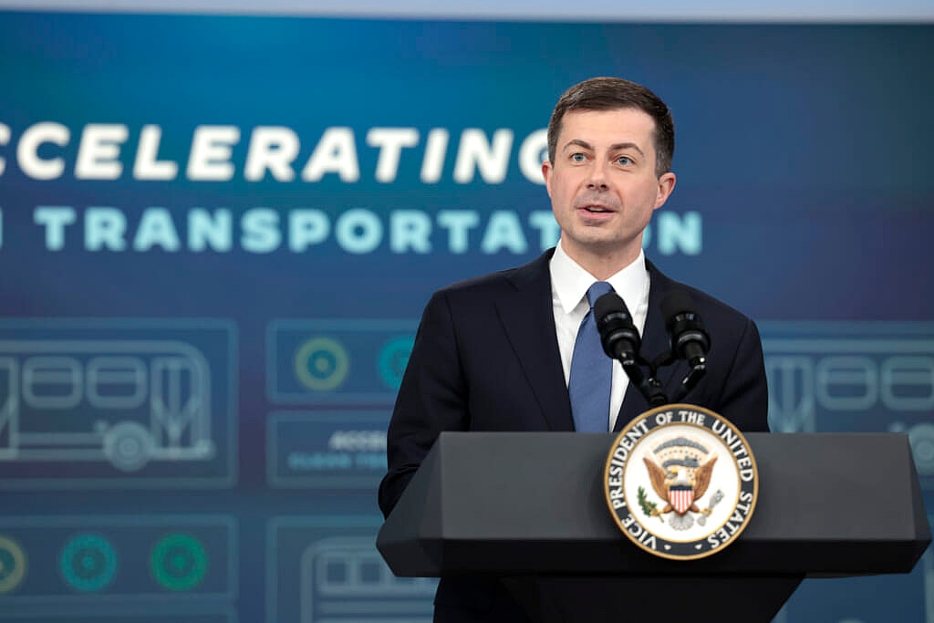 Secretary of the Department of Transportation Pete Buttigieg behind a podium wearing a black suit and blue tie