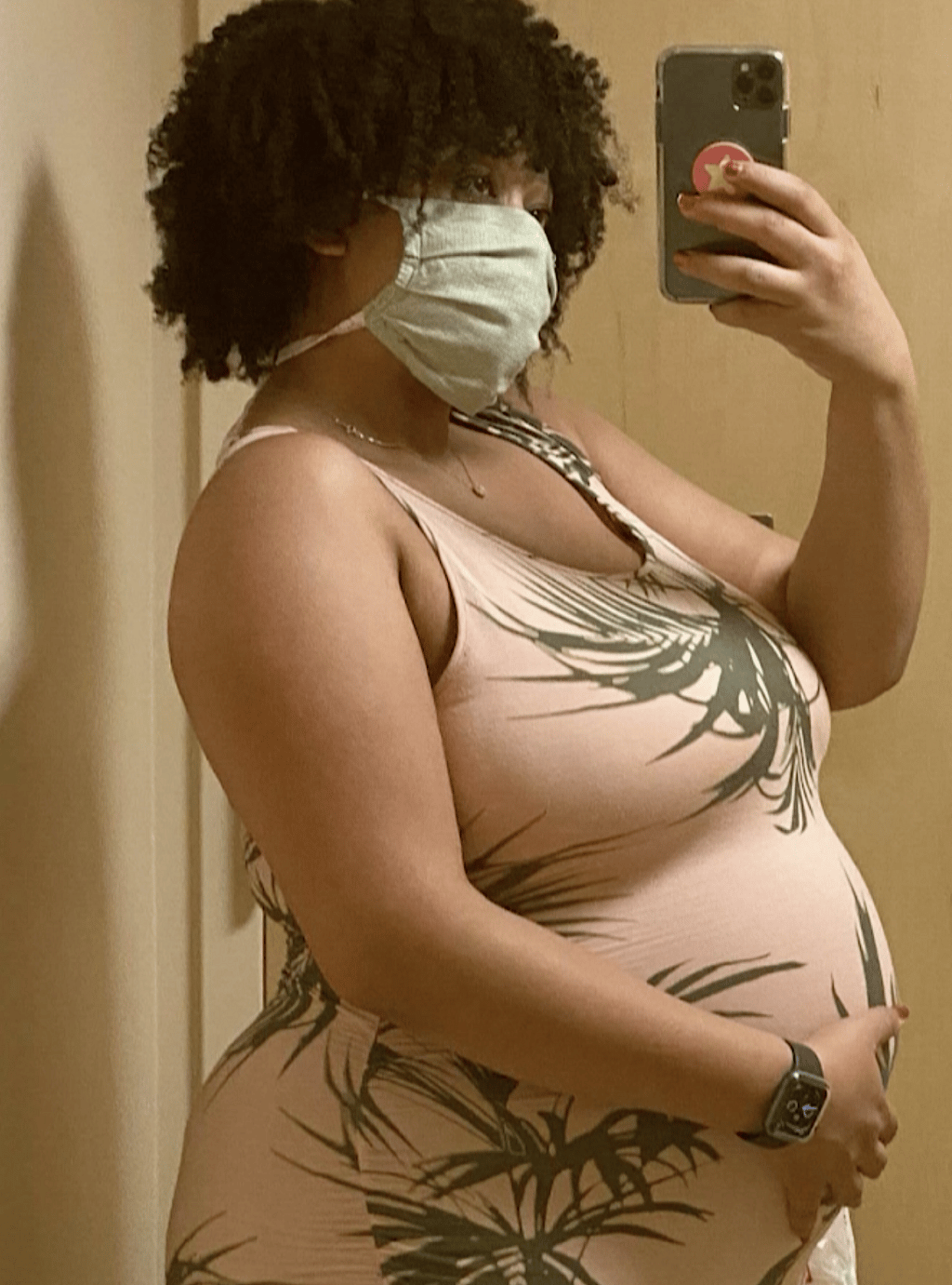 A pregnant woman wearing a face mask holds up a cell phone