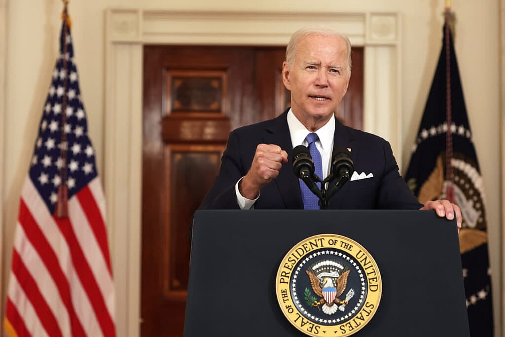 President Joe Biden stands behind a podium wearing a black suit and blue tie