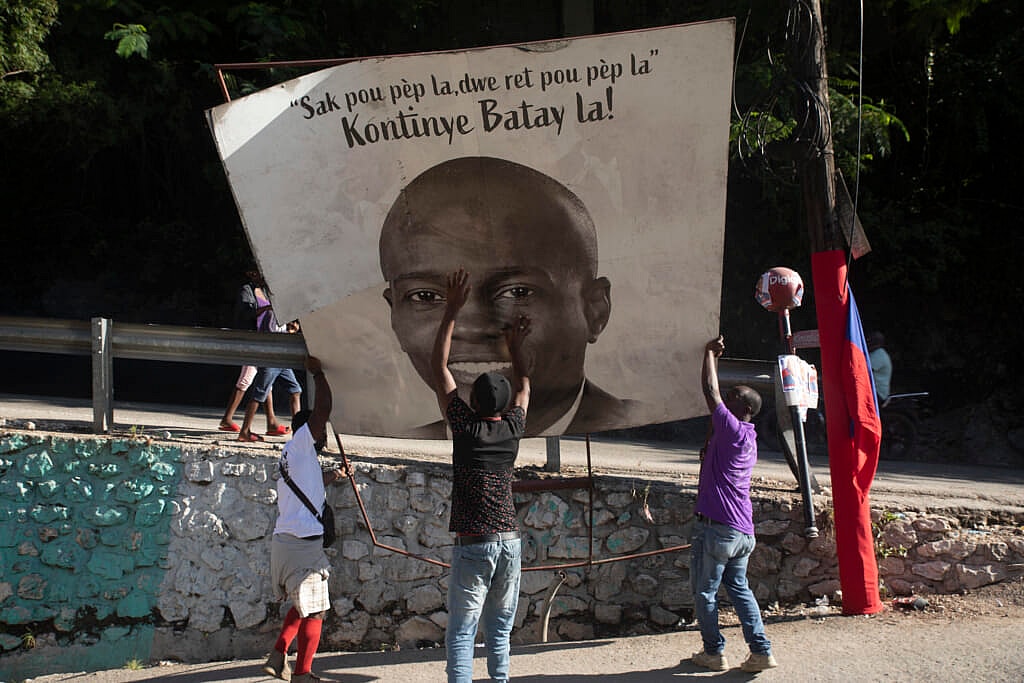 Three people raise a sign portraying slain Haitian President Jovenel Moise